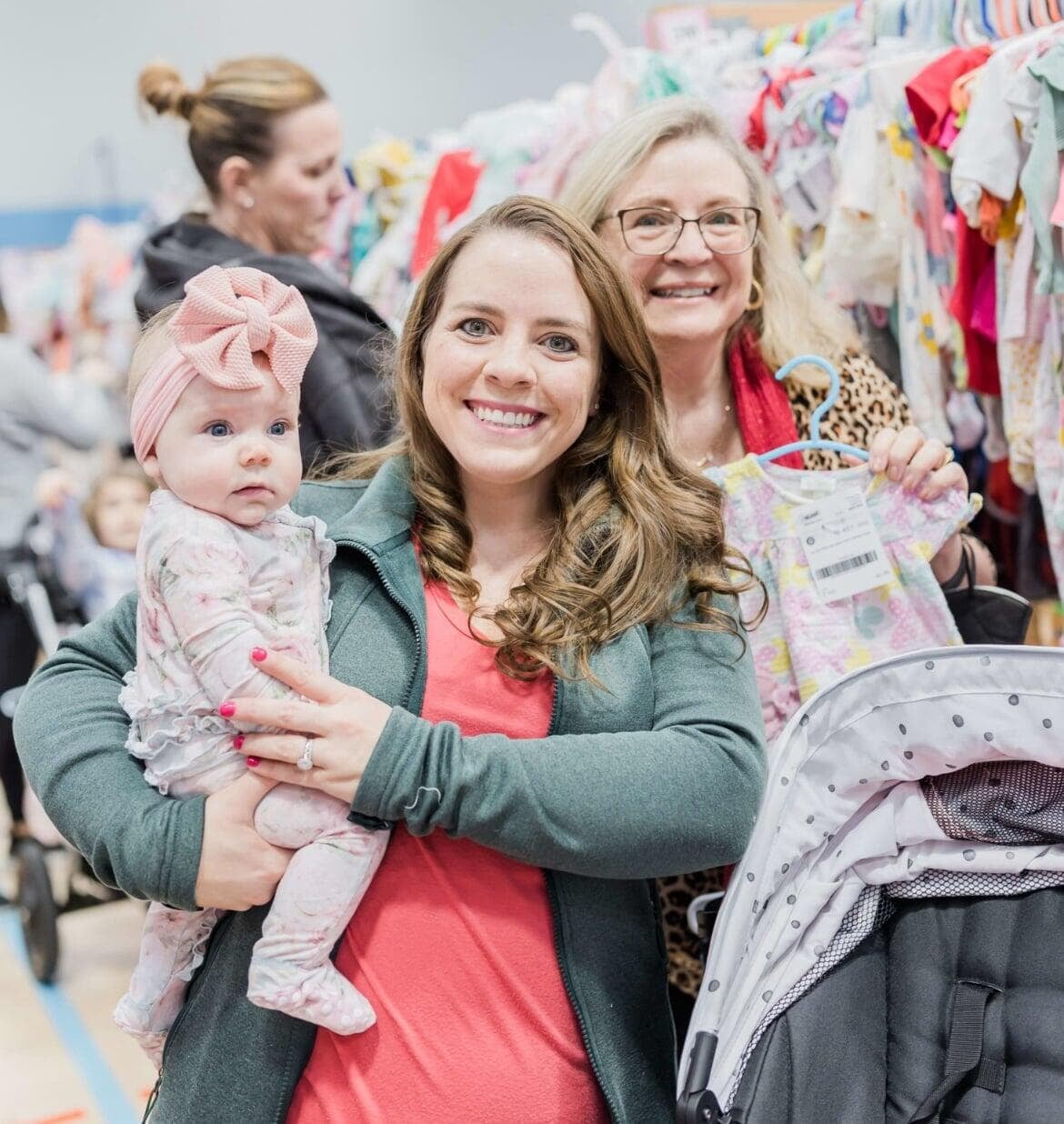 Mom holds hand up to show of rows and rows of clothing for sale at 50 to 90% off retail prices!