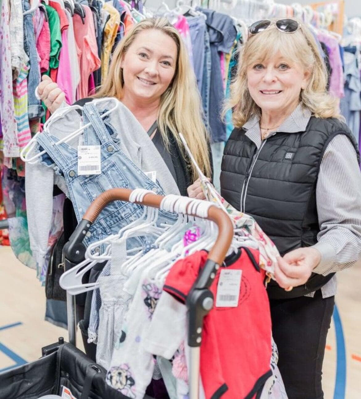 A mom and grandmother stand beside a rack of clothing.