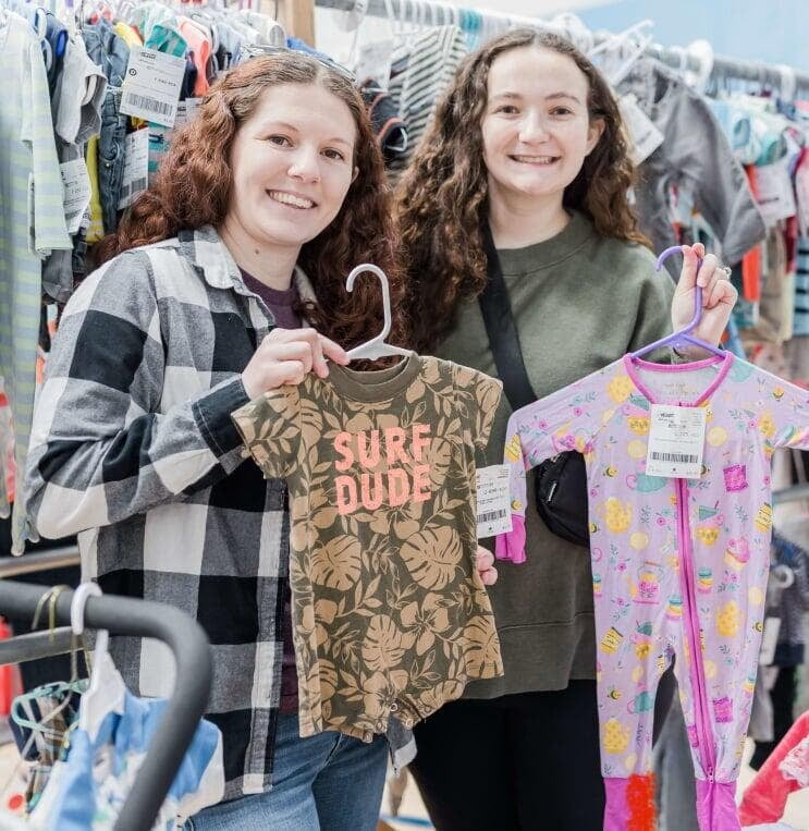 Two moms holding baby clothing